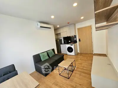 Modern living room with compact kitchen and washing machine, featuring sleek design and wooden flooring.