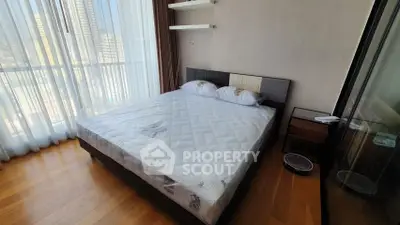 Modern bedroom with large window and hardwood floors in a high-rise apartment.