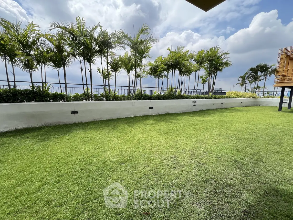 Spacious garden area with lush green lawn and palm trees under a cloudy sky.