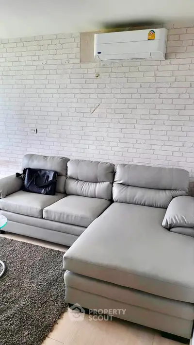 Modern living room with stylish gray sectional sofa and white brick wall, featuring a sleek air conditioning unit.