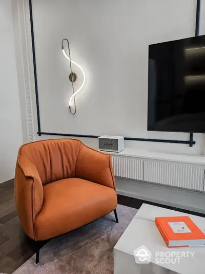 Chic modern living space featuring a plush burnt orange accent chair, sleek wall-mounted TV, and artistic lighting fixture, perfect for urban living.