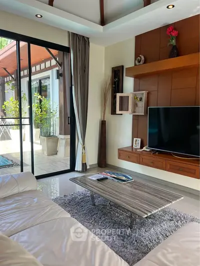 Luxurious living room with modern decor, large TV, and sliding glass doors opening to a sunny patio.