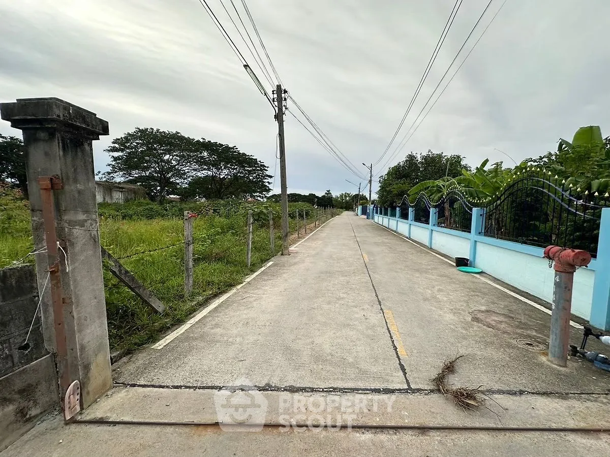 Charming rural road with lush greenery and blue fence, perfect for serene countryside living.