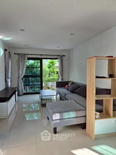 Spacious living room with modern furniture and large window offering natural light and garden view.