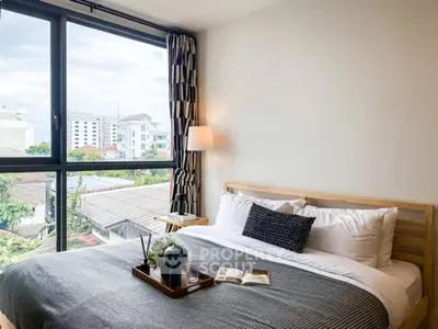 Modern bedroom with large window offering city view, stylish decor, and cozy ambiance.