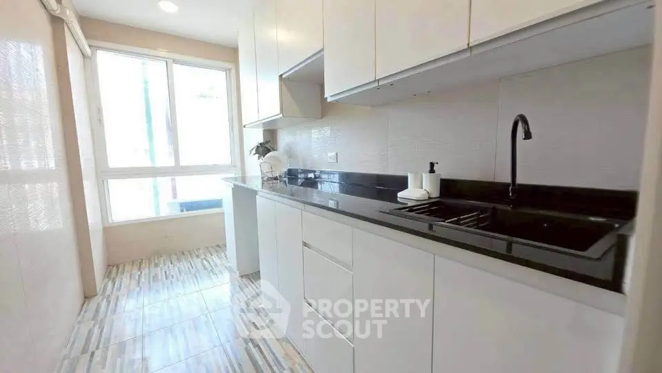 Modern kitchen with sleek white cabinets and black countertop, featuring a large window for natural light.
