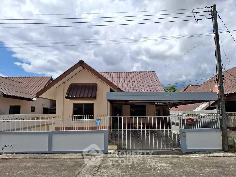 Charming single-story house with gated driveway and tiled roof under a cloudy sky.
