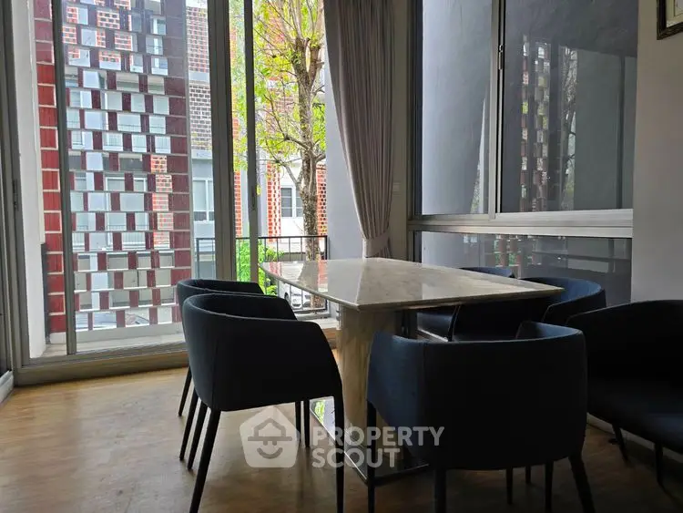 Modern dining area with sleek table and chairs, large windows offering natural light and urban view.