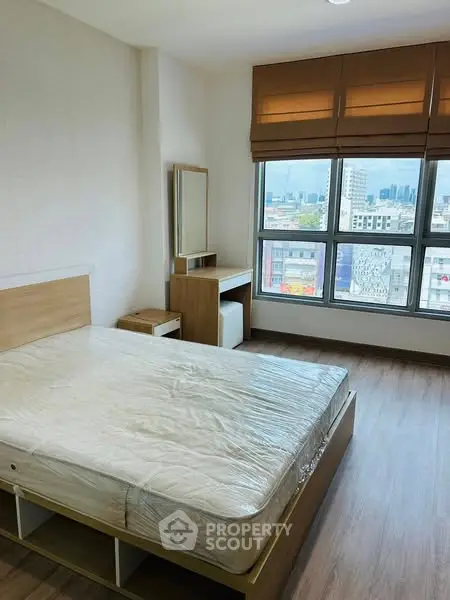 Spacious bedroom with large window offering city views, featuring modern furnishings and wooden flooring.