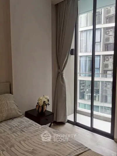 Modern bedroom with floor-to-ceiling window and city view, featuring elegant decor and natural light.