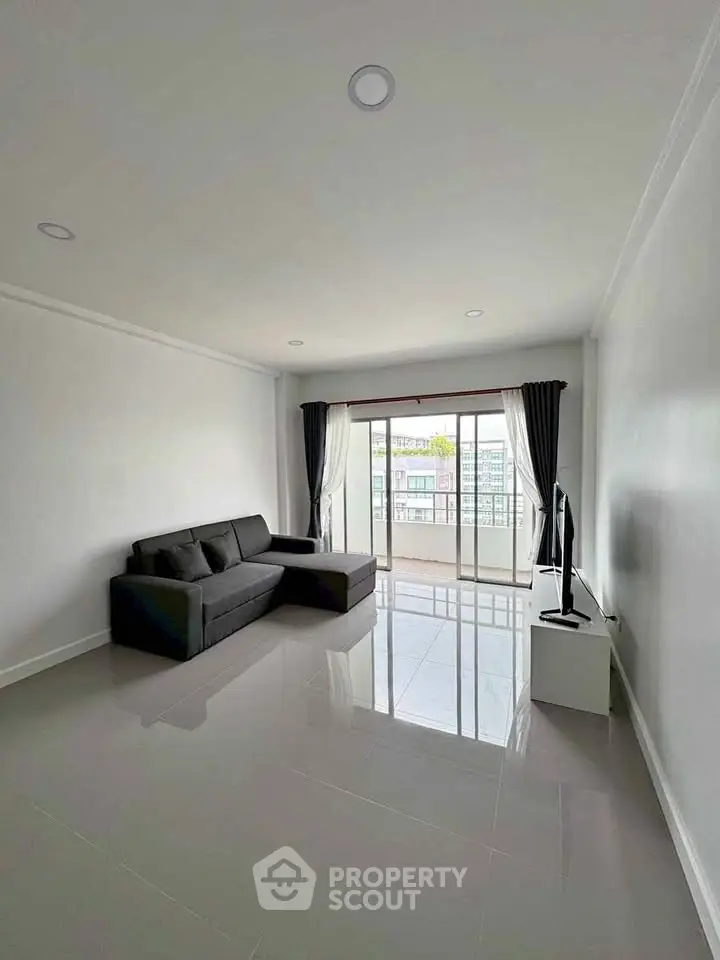 Spacious living room with sleek sofa and large window offering natural light and balcony access.
