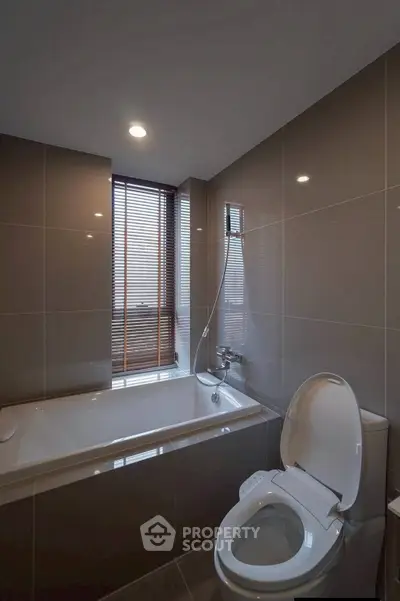 Modern bathroom with sleek bathtub and toilet, featuring elegant tile design and natural light.