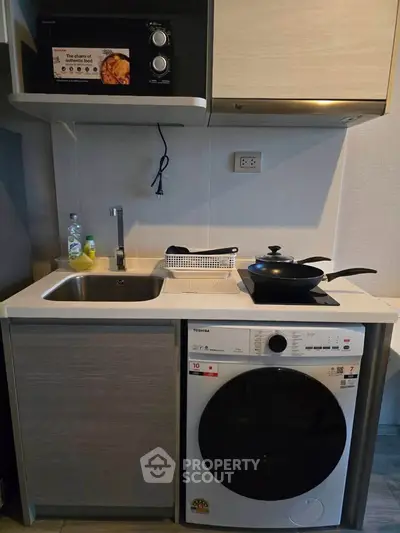 Compact modern kitchen with sink, microwave, and washing machine in small apartment.