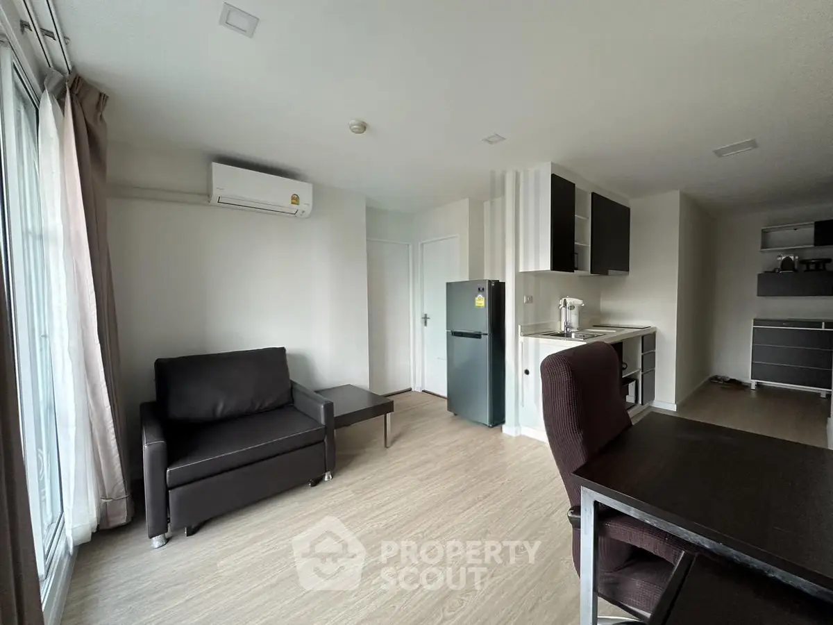 Modern living room with sleek furniture and compact kitchen in open layout apartment.