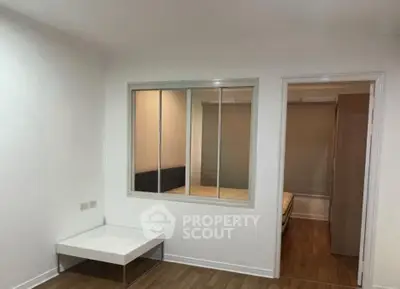 Minimalist bedroom with wooden flooring and a small side table, featuring a window to an adjacent room.