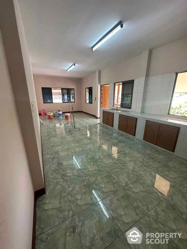 Spacious kitchen with polished green marble flooring and ample natural light, featuring built-in wooden cabinets and modern fluorescent lighting.