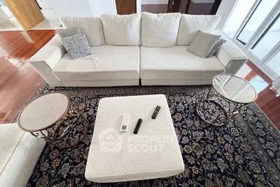 Elegant living room with plush white sofa, stylish side tables, and a luxurious patterned rug on polished wooden floors.