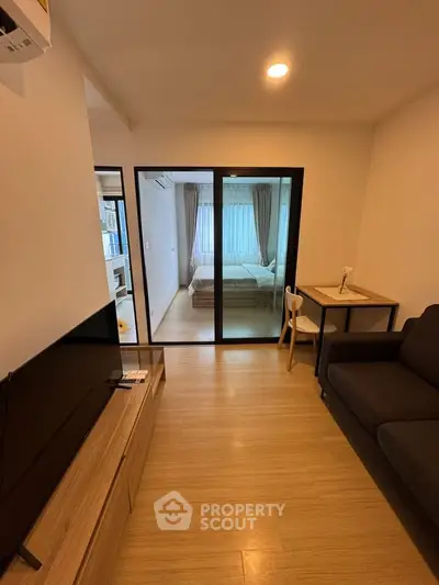 Modern apartment interior with cozy living room and view into a stylish bedroom through glass doors.