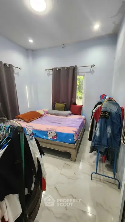Cozy bedroom with natural light and marble flooring, featuring a bed and clothing racks.