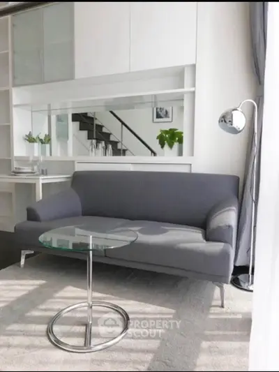 Modern living room with sleek gray sofa and glass coffee table, featuring stylish decor and natural light.