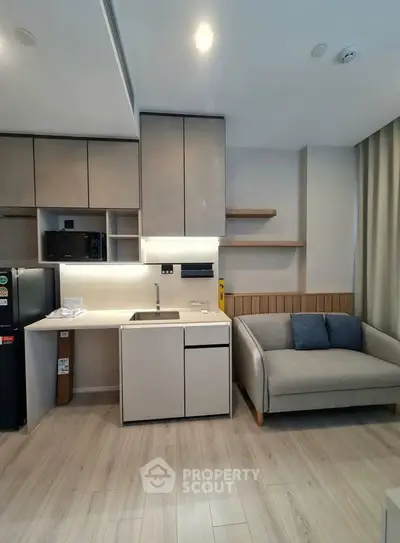Modern compact kitchen with sleek cabinetry and cozy living area in a stylish apartment.