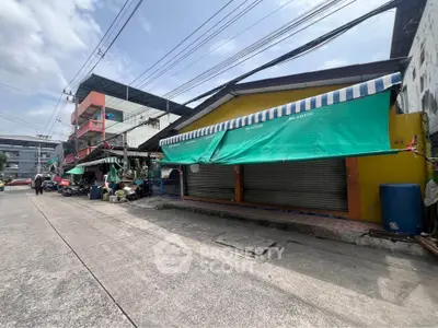 Street view of commercial buildings with closed shutters and colorful awnings.