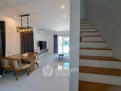 Spacious modern living room with dining area and staircase, featuring elegant lighting and contemporary decor.