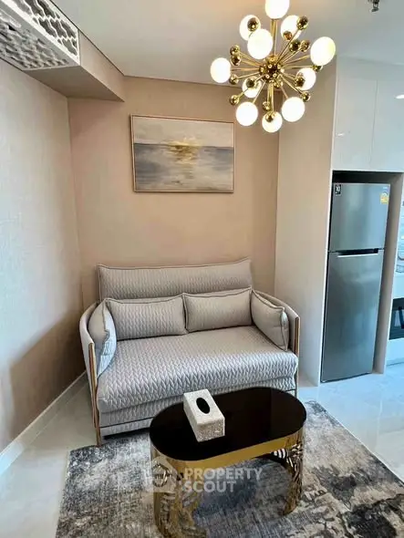 Modern living room with elegant sofa, stylish chandelier, and sleek refrigerator in a cozy apartment setting.