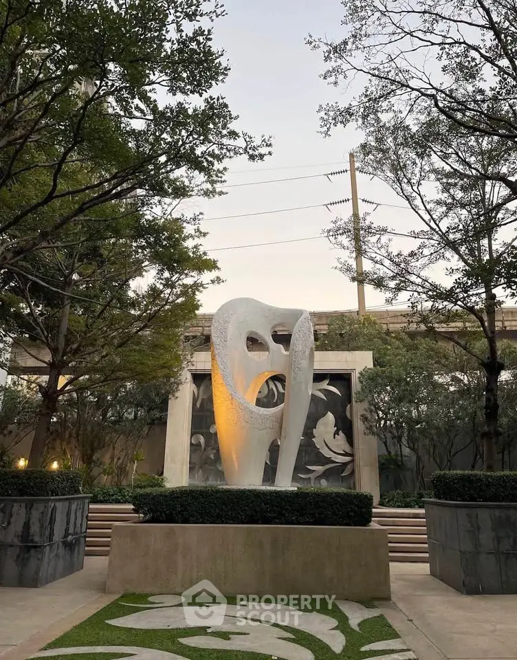 Elegant garden with modern sculpture and lush greenery in upscale residential complex.