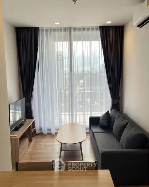 Modern living room with large window and stylish furniture in high-rise apartment.