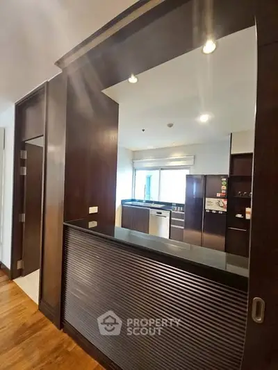 Modern kitchen with open layout and sleek dark wood finishes, featuring stainless steel appliances and ample natural light.