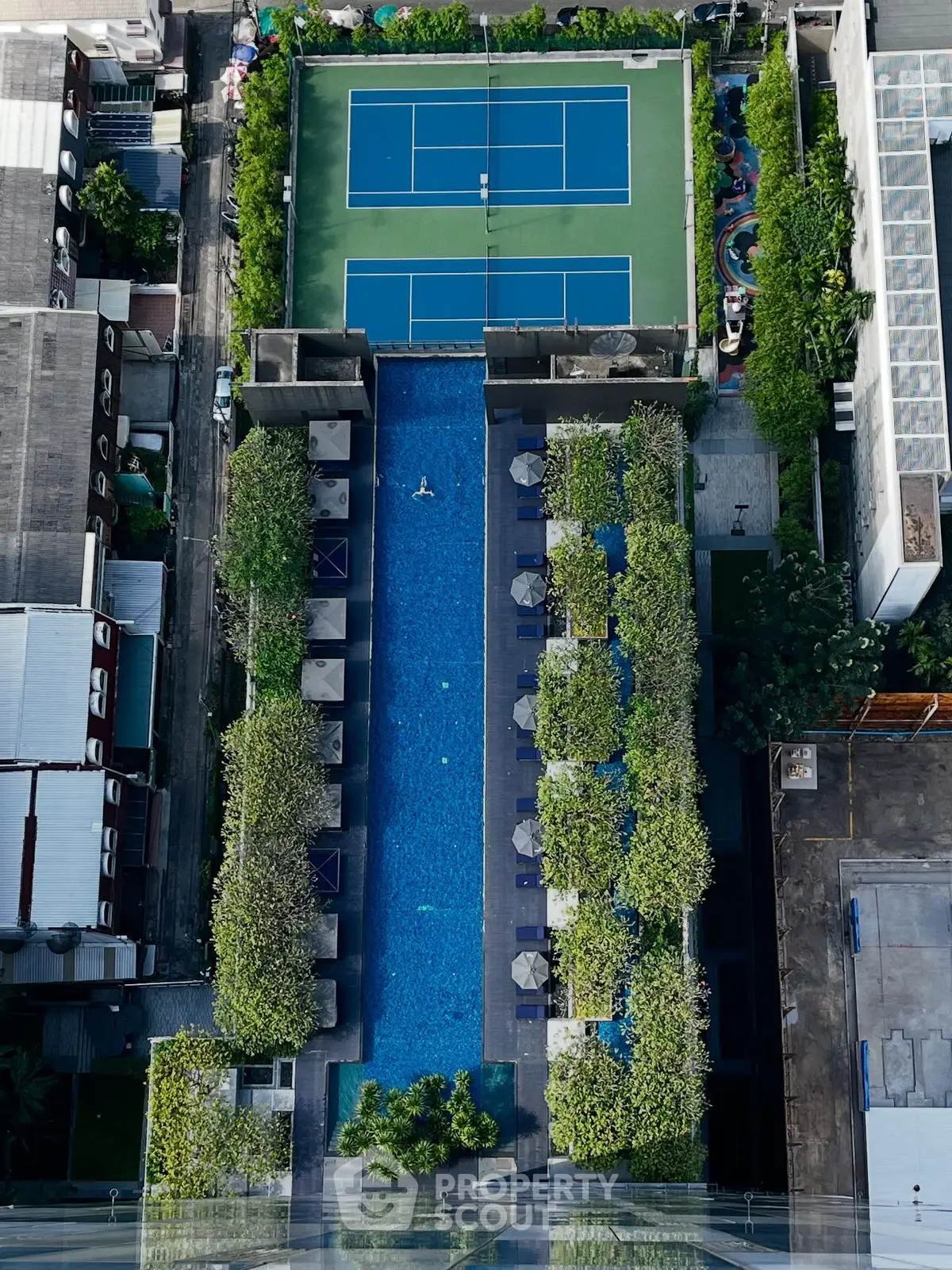 Stunning aerial view of luxury rooftop pool and tennis court in urban setting.