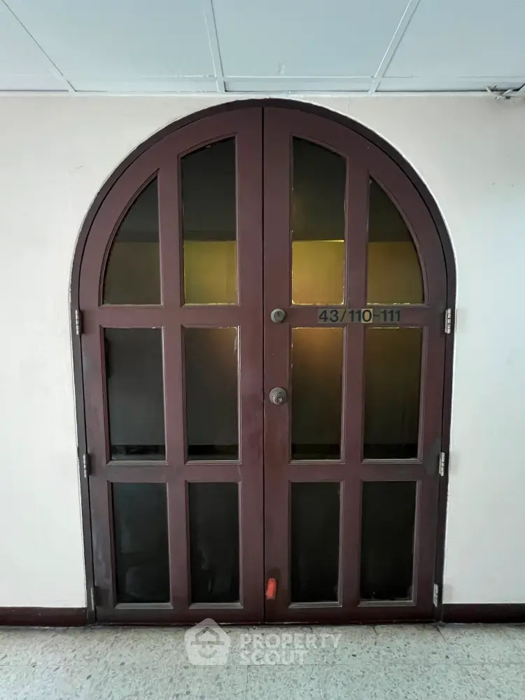 Unique arched wooden door with frosted glass panels in a residential building hallway.