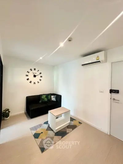 Modern living room with sleek black sofa, stylish clock, and air conditioning in a bright, minimalist space.