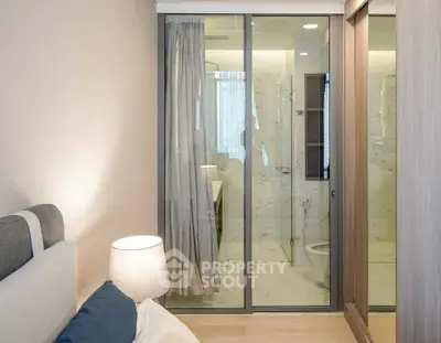 Modern bedroom with glass partition to ensuite bathroom, featuring sleek design and cozy ambiance.
