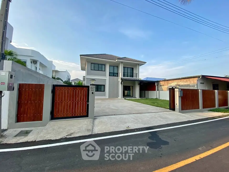 Modern two-story house with spacious driveway and wooden gate in a suburban neighborhood.