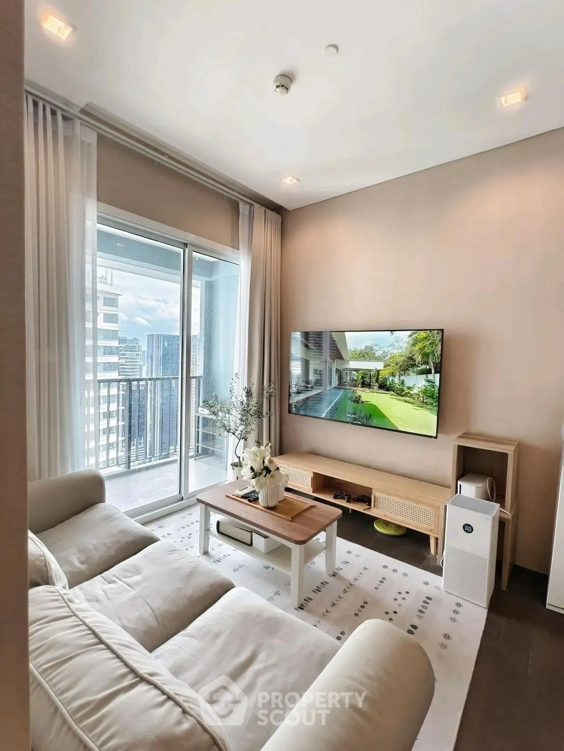 Modern living room with balcony view, cozy sofa, and wall-mounted TV in a high-rise apartment.