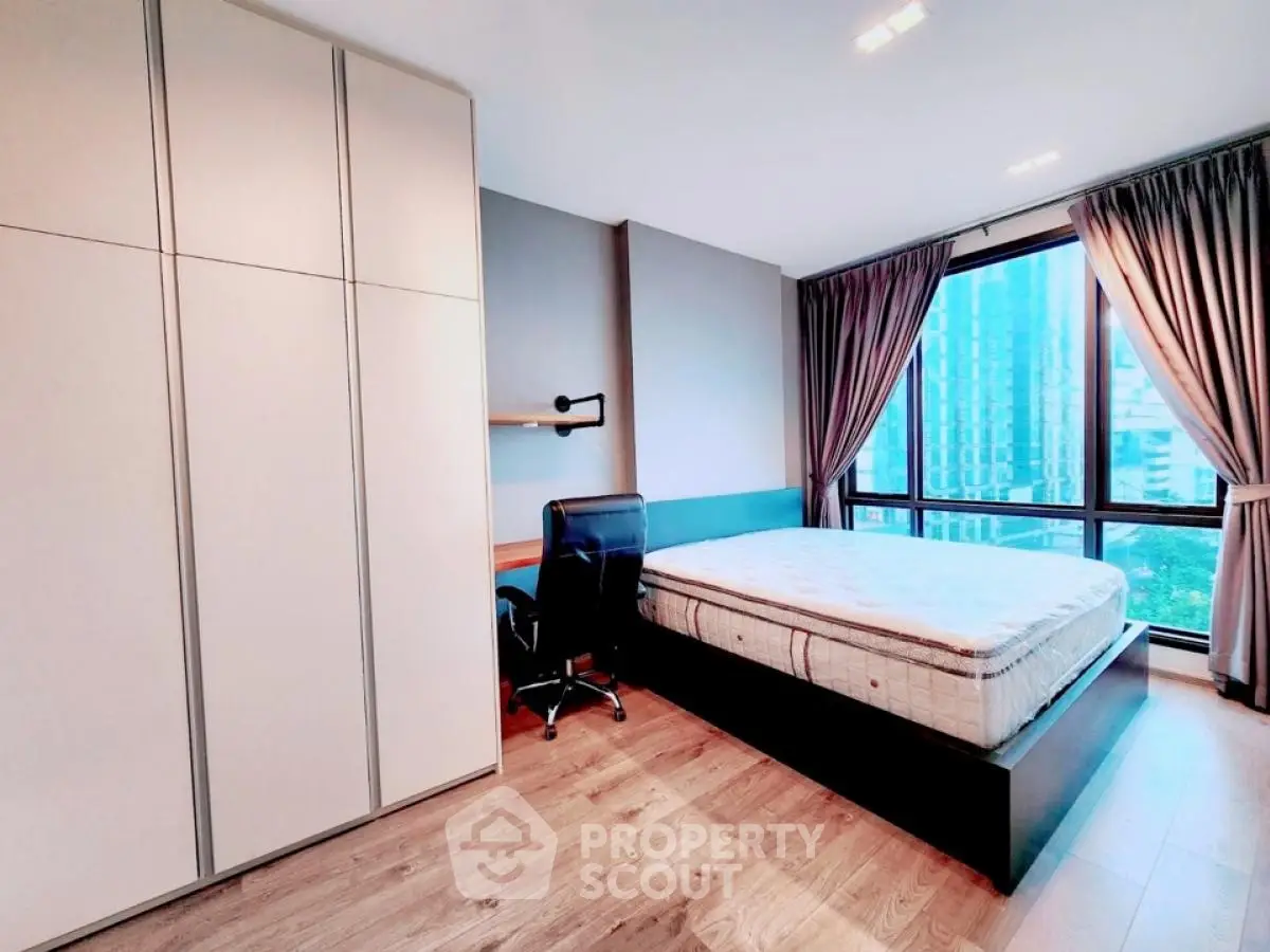 Modern bedroom with large window and city view, featuring sleek furniture and wooden flooring.