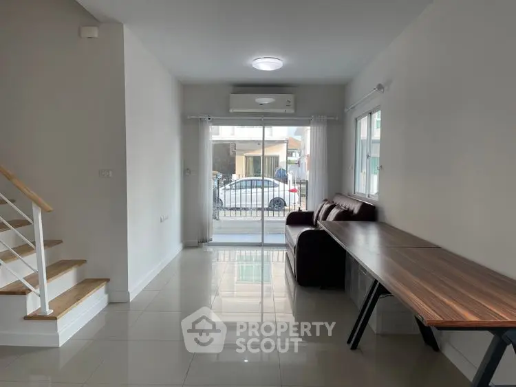 Modern living room with sleek design and natural light, featuring a staircase and large windows.