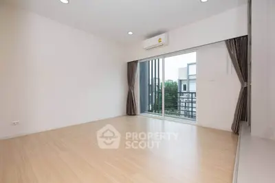 Spacious empty room with wooden flooring and balcony view in modern apartment