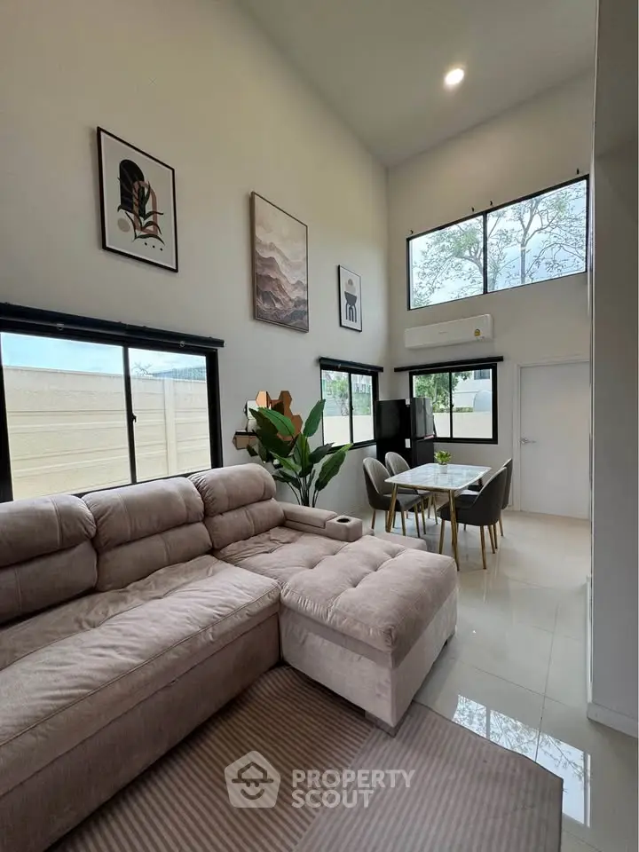 Spacious modern living room with high ceilings and large windows, featuring a cozy sectional sofa and elegant dining area.