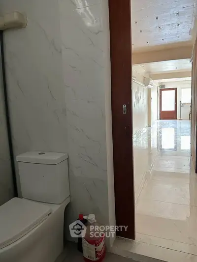 Spacious hallway with glossy tiles leading to a bright entrance, adjacent to a modern bathroom.