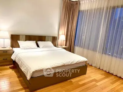 Elegant bedroom with wooden flooring and large window in modern apartment.