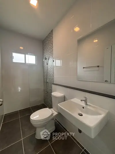 Modern bathroom with sleek fixtures and tiled walls, featuring a shower and large window for natural light.