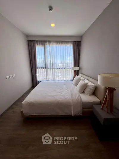 Spacious bedroom with large window offering stunning city views, modern decor, and cozy ambiance.