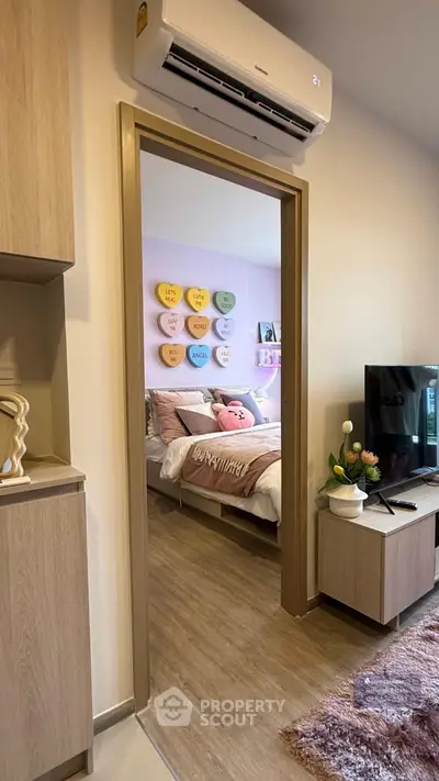 Cozy bedroom with pastel decor and modern living room view, featuring air conditioning and stylish furnishings.