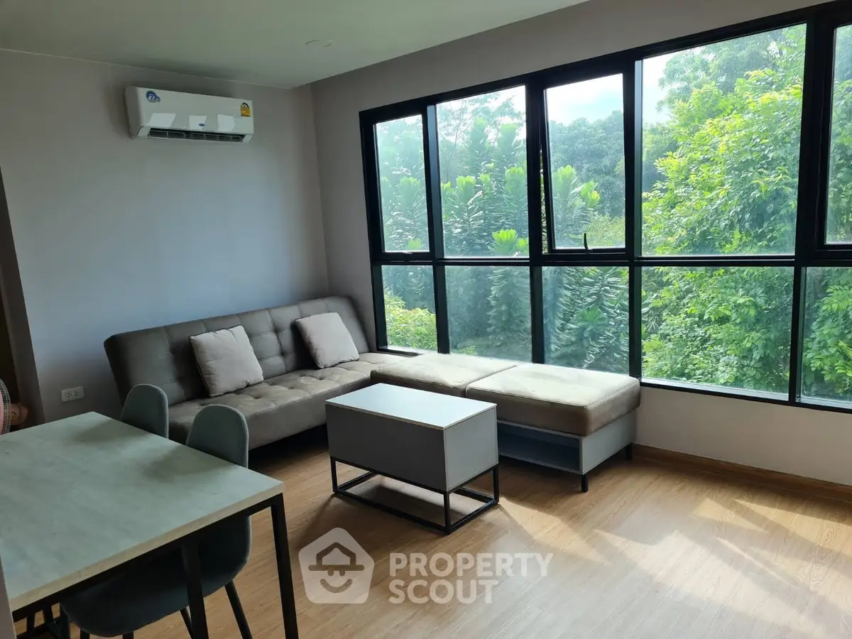 Modern living room with large windows and lush green view, featuring a cozy sofa and dining area.