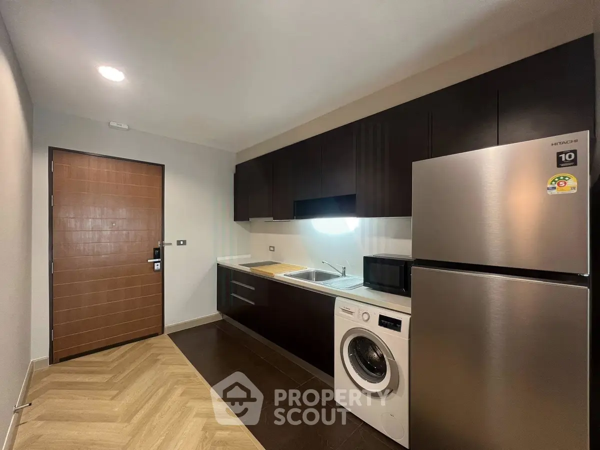 Modern kitchen with sleek cabinets, washing machine, and stainless steel fridge.