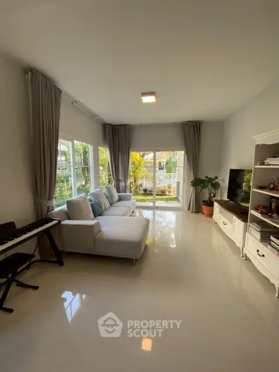 Spacious living room with large windows and garden view, featuring modern furniture and natural light.
