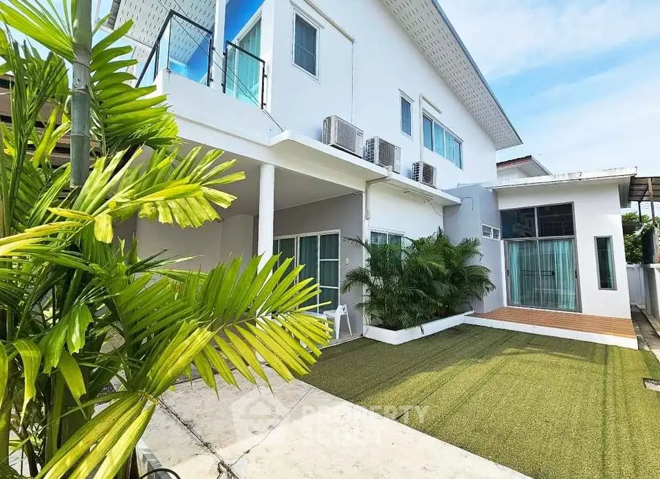 Modern white two-story house with lush greenery and spacious outdoor area.